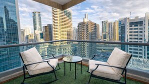 Ein Balkon mit zwei Stühlen und einem kleinen Tisch, mit Blick auf eine Skyline moderner Hochhäuser.