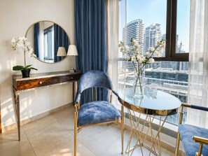 Ein modernes Zimmer mit blauem Sessel, rundem Tisch, Spiegel und Blick auf StadtgebÀude.