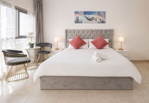 Une chambre d’hôtel avec un grand lit, deux oreillers, une table de chevet avec une lampe, une chaise et une fenêtre avec des rideaux.