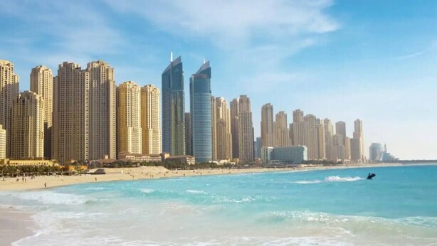 Un paysage urbain côtier avec de hauts immeubles, une plage et un jet ski sur l’eau.