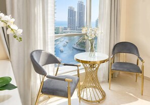 A modern room with two grey upholstered chairs, a gold-framed round table, and a view of a cityscape through large windows.