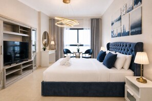 A modern hotel room with a large bed, a television, a desk, and a dining area.