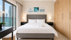 A modern hotel room with a large bed, two bedside tables with lamps, a view of the city, and artwork on the wall.