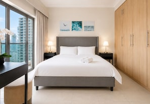 Une chambre d’hôtel moderne dotée d’un grand lit, de deux tables de chevet avec des lampes, d’une vue sur la ville et d’œuvres d’art accrochées au mur.