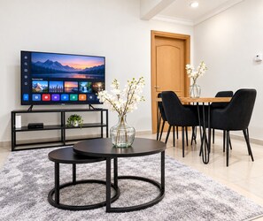 Ein modernes Wohnzimmer mit einem Flachbildfernseher, einem Esstisch mit Stühlen, einer Vase mit Blumen und einem Bücherregal.