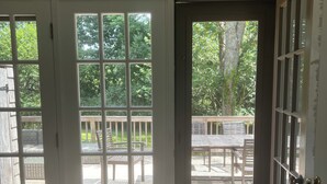 Ein Zimmer mit einer großen Schiebeglastür, die auf eine Terrasse mit Holzmöbeln und Blick auf Bäume führt.