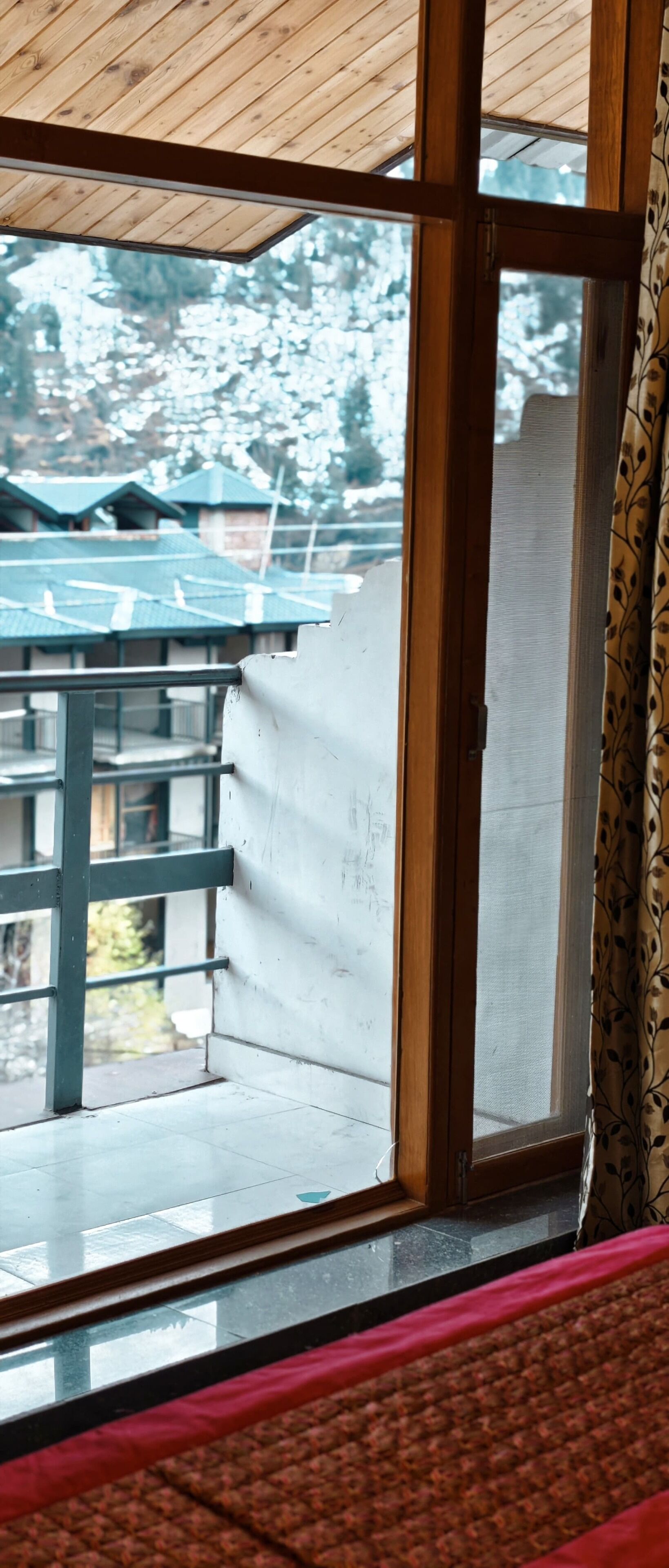 A room with a large window, a wooden ceiling, and a view of buildings outside.