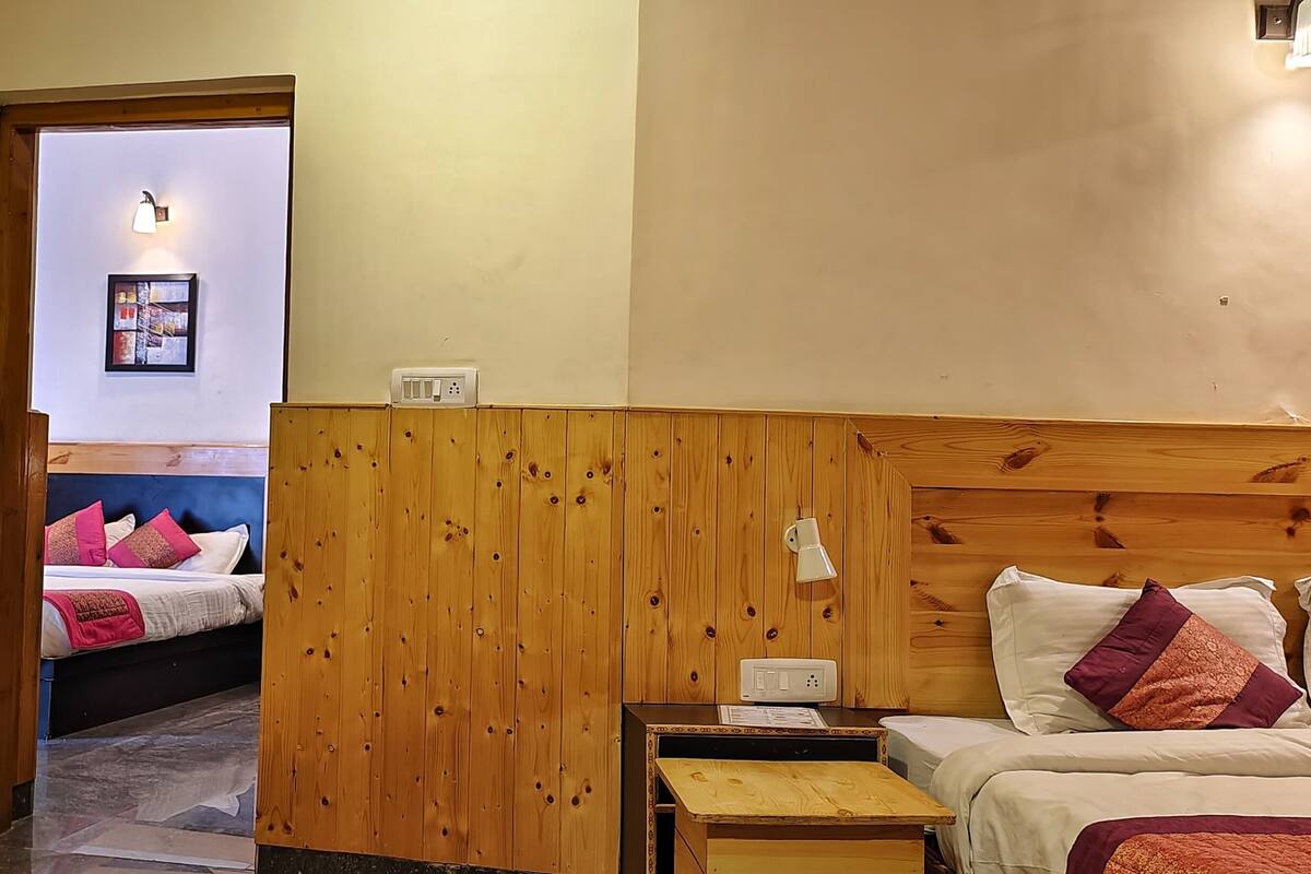 A hotel room with wooden paneling, a bed with multiple pillows, a bedside table, and a wall-mounted light fixture.