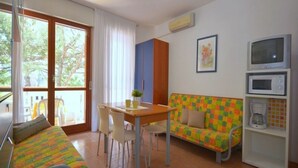 Una habitación con una cama, una mesa con sillas, un sofá colorido, un televisor y un microondas.