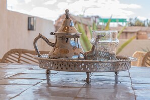Una tetera plateada con tapa y un vaso sobre una bandeja, colocada en una mesa con azulejos.