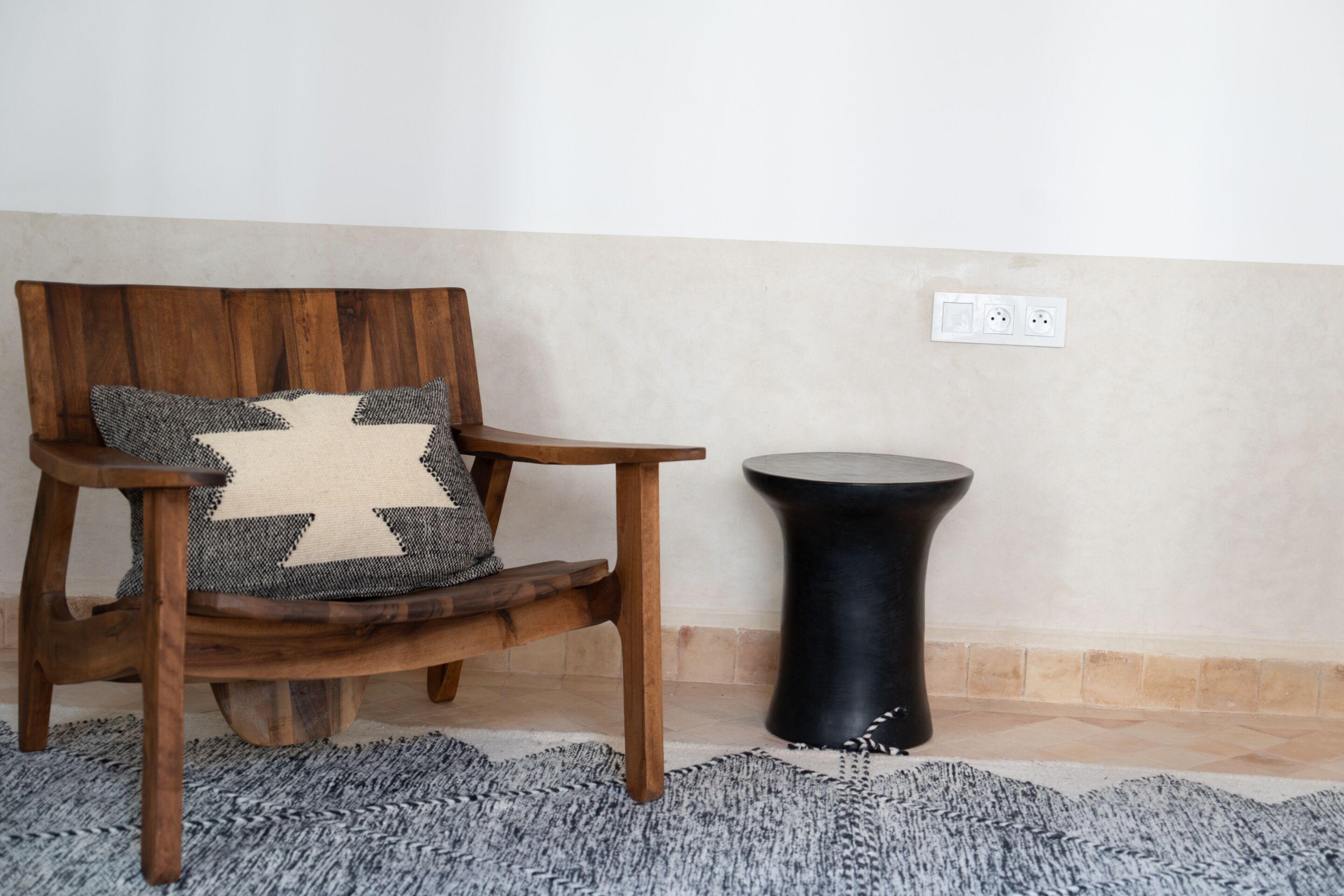 Una silla de madera con un cojín estampado y una mesita auxiliar negra.