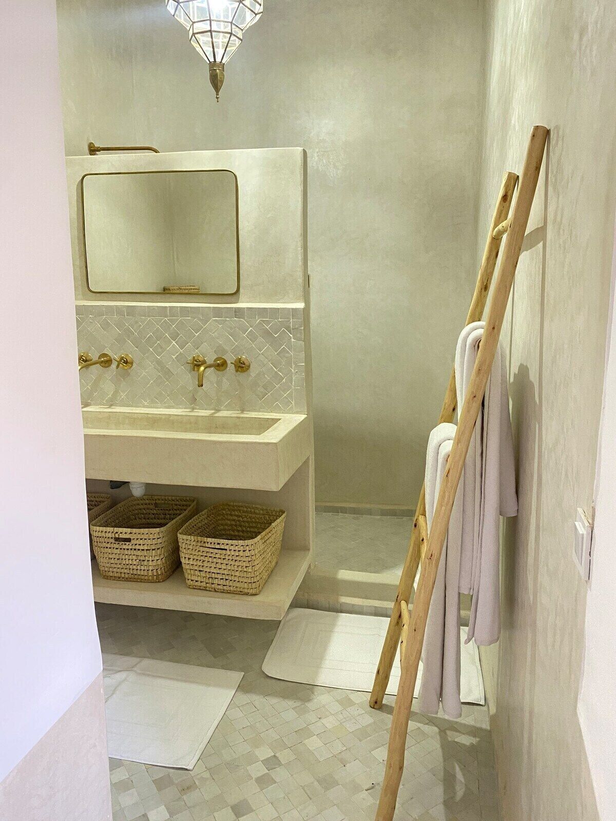 A bathroom with a white vanity, a mirror, a shower area, and a wooden ladder leaning against the wall.