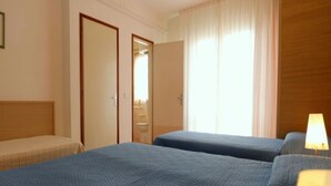 Ein Hotelzimmer mit zwei Betten, einem Holzkopfstück, einem Fenster mit Vorhängen und einer Nachttischlampe.