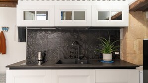 Een keuken met een zwart aanrechtblad, witte kastjes en een decoratieve achterwand.