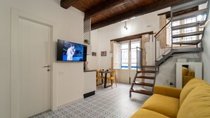 Een woonkamer met een televisie, een gele bank, een trap en een eethoek.