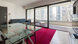 A modern living room with a glass table, a red carpet, and a balcony with a view of buildings. - GuestHost - Modern apartment with balcony in Portello district (Milano)