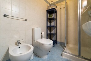 A bathroom with a bidet, toilet, shower, and a shelf with a basket. - GuestHost - Charming Apartment in the Heart of Ortigia (Siracusa)
