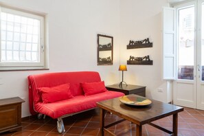 A room with a red sofa, a wooden table, a lamp, and wall art. - GuestHost - Charming Apartment in the Heart of Ortigia (Siracusa)