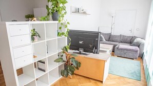 Ein modernes Wohnzimmer mit einer weißen Regaleinheit, einem Schreibtisch mit Computer, einem grauen Sofa und einem grünen Teppich.