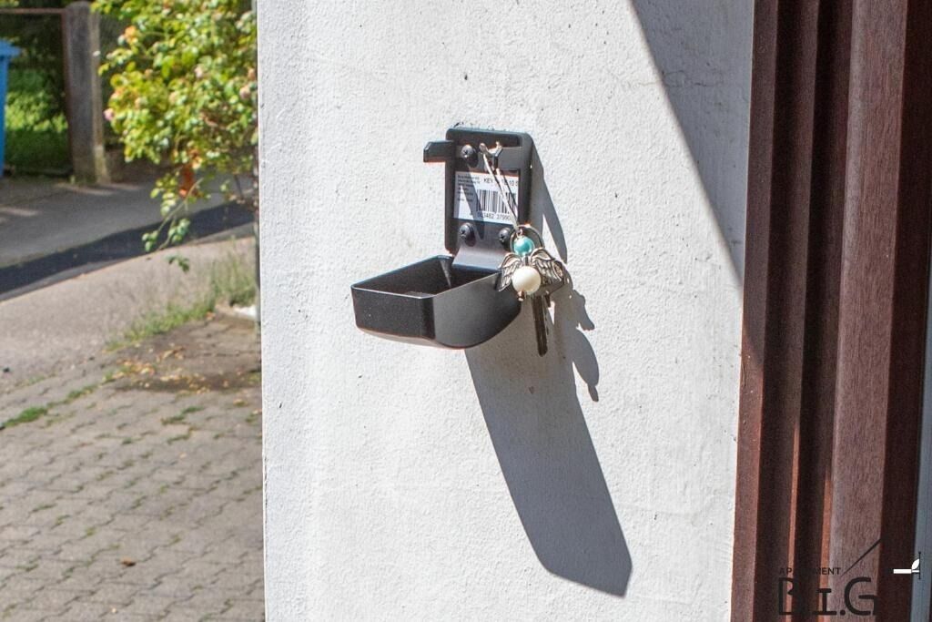 Un buzón exterior fijado a la pared, con llave y un pequeño contenedor adjunto.