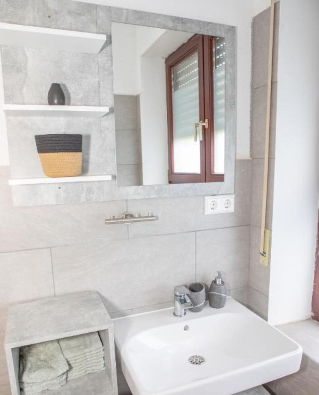 Une salle de bain avec un lavabo blanc, un miroir et une fenêtre avec des stores.