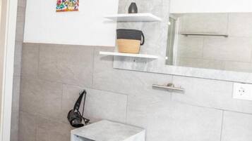 Une salle de bain moderne avec des carreaux gris, un lavabo blanc, un miroir et une étagère sur laquelle se trouve un panier.