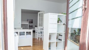 Ein Zimmer mit einem Bett, einem Schreibtisch, einem Stuhl und einem weißen Regal mit Pflanzen.