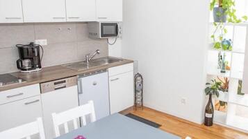 A modern kitchen with white cabinets, a built-in microwave, and a coffee maker. There is a dining table with a vase of flowers.