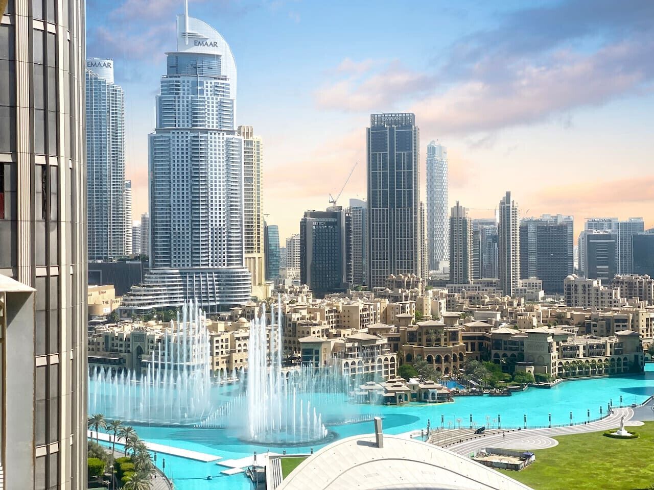 A cityscape with high-rise buildings, a large fountain, and a body of water.