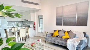 Una sala de estar moderna con un sofá gris, una mesa de centro de vidrio y un comedor con sillas blancas.