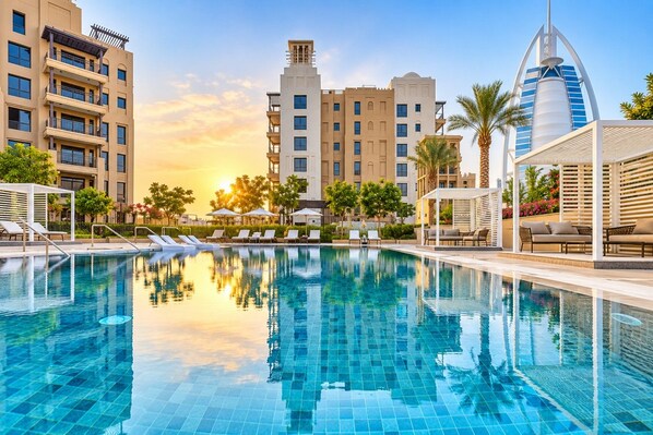 A swimming pool with lounge chairs, a sunken seating area, and modern buildings in the background.