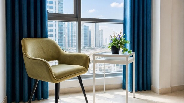 A room with a view of a cityscape through large windows, a single chair, a small table, and a potted plant. - Cozy Studio at Marina near Beach & Metro in Marina (Dubai)