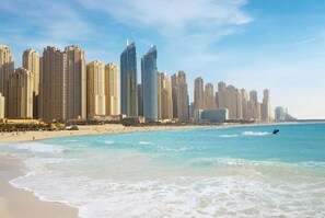 Un paysage urbain côtier avec de hauts immeubles, une plage de sable et un ciel bleu dégagé.