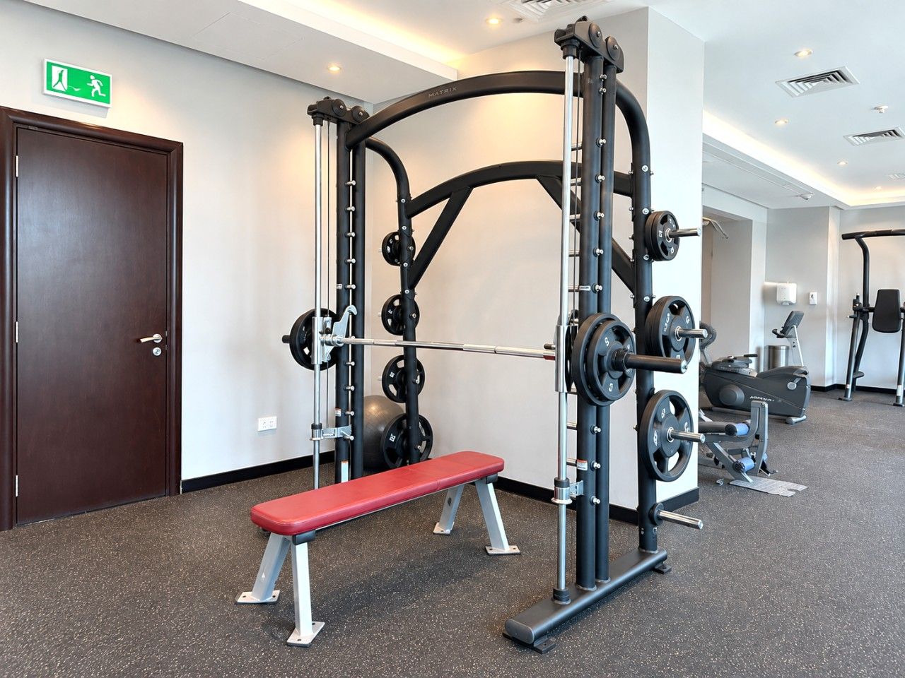 Un gimnasio con banco, equipo de levantamiento de pesas y cinta de correr.