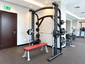 Une salle de sport équipée d’un banc, de matériel de musculation et d’un tapis de course.