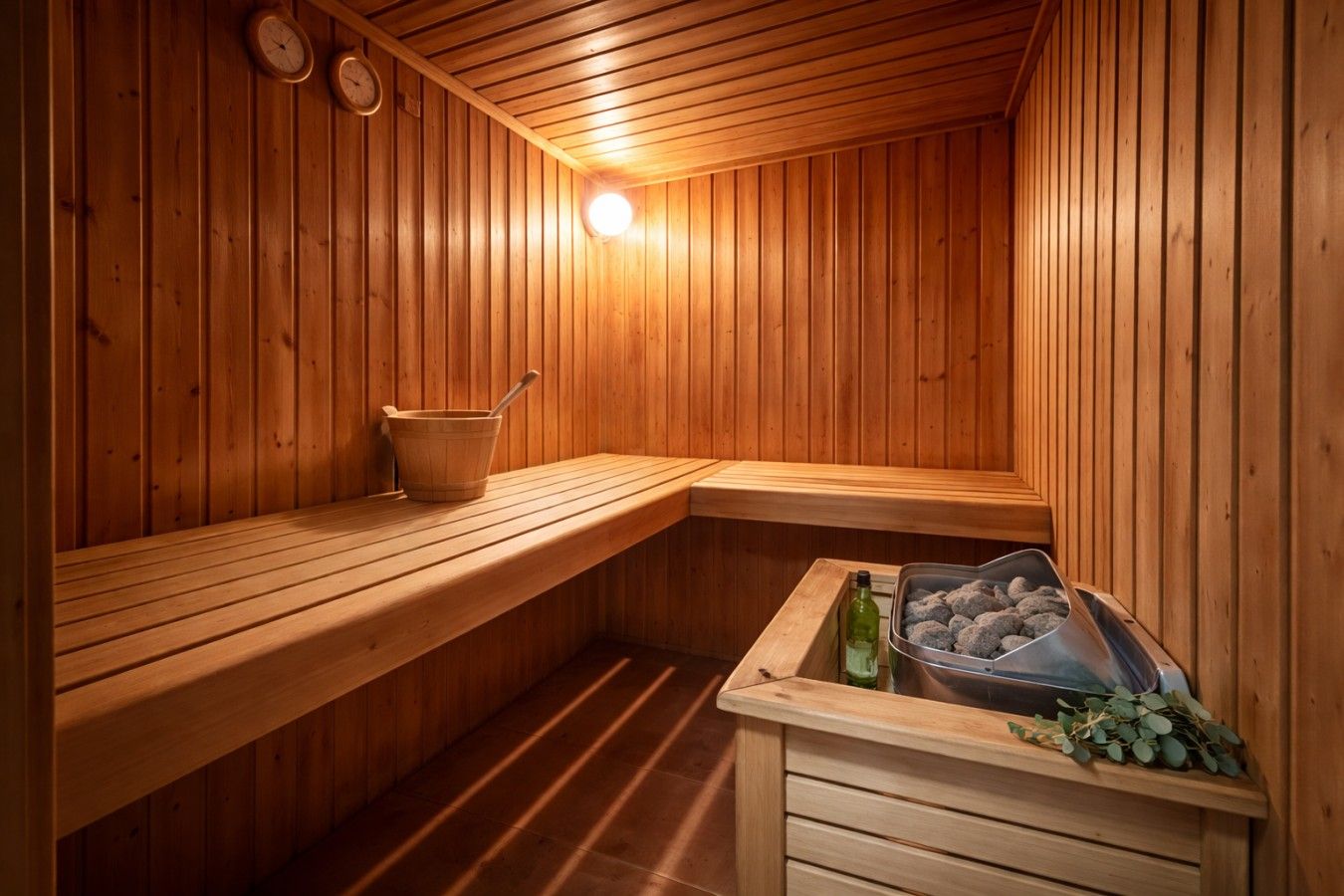 A sauna with wooden benches, a bucket, and a container with stones.