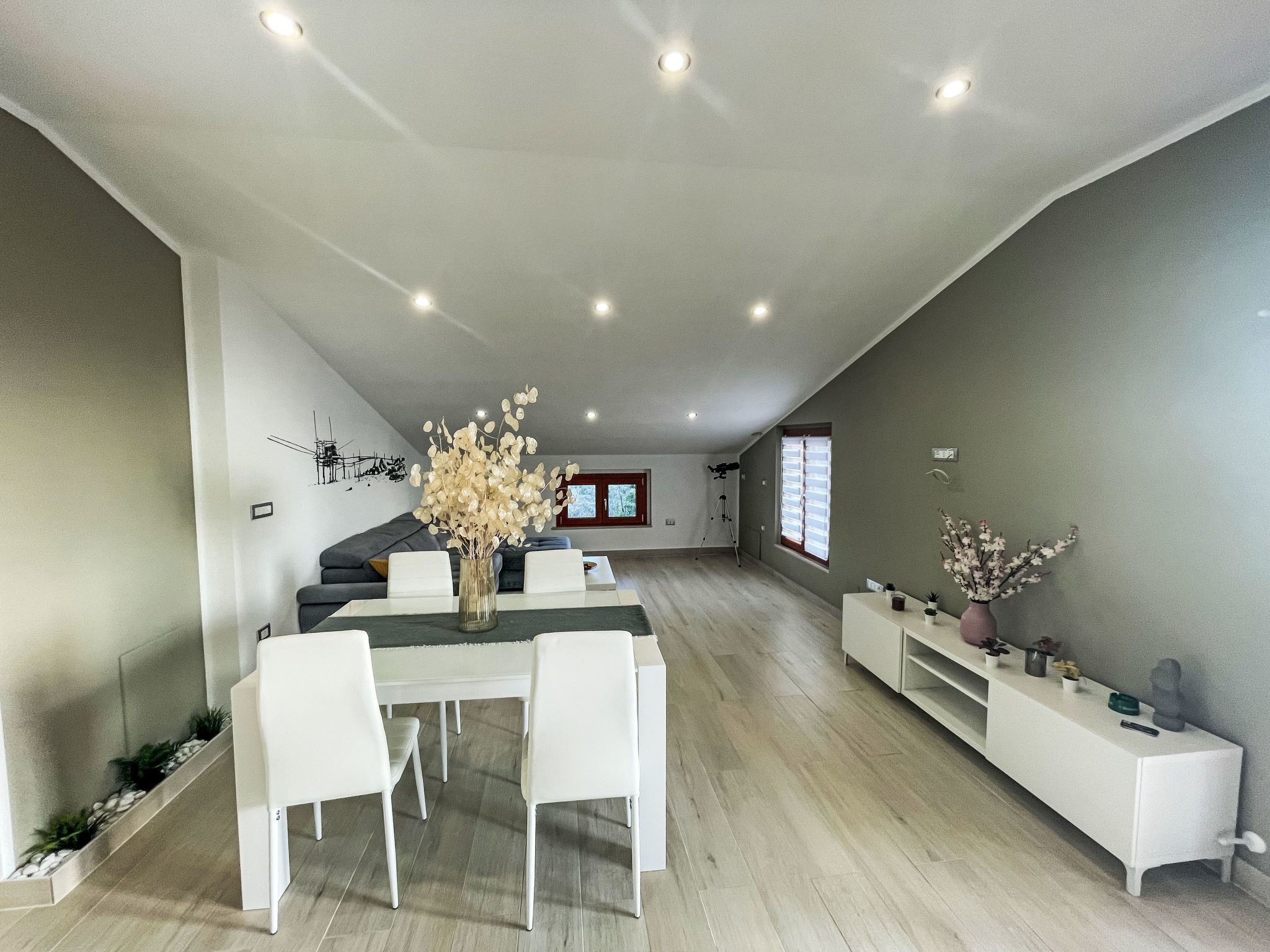 A modern living room with a dining area, featuring a white sofa set, a dining table with chairs, and a vase with flowers.