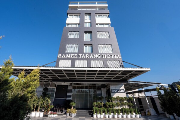 The Ramee Tarang Hotel with a modern facade, large windows, and a covered entrance area with potted plants.