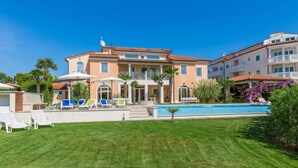 A large, multi-story building with a swimming pool, outdoor seating, and a well-maintained lawn.