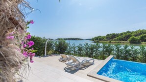 A pool area with two lounge chairs and a view of a lake and forest.