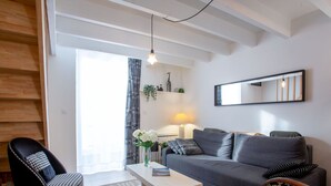 Un salon moderne avec un canapé gris, des fauteuils à motifs, une table basse blanche et un luminaire suspendu.