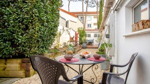 Une terrasse avec deux chaises et une table, entourée d’une haie et d’un bâtiment.