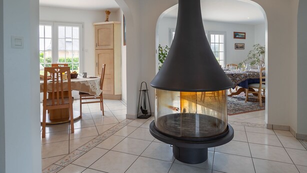 A spacious room with a large fireplace, a dining area with a table and chairs, and a view of the outdoors through large windows. - Ty Stella by Interhome (Porspoder)