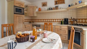 A kitchen with wooden cabinets, a tiled backsplash, and a dining table set with bread, pastries, and a bottle of juice. - Ty Stella by Interhome (Porspoder)