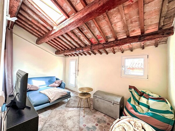 Ein gemütliches Zimmer mit einem blauen Sofa, einem Fernseher, einem kleinen Tisch und einem Fenster.