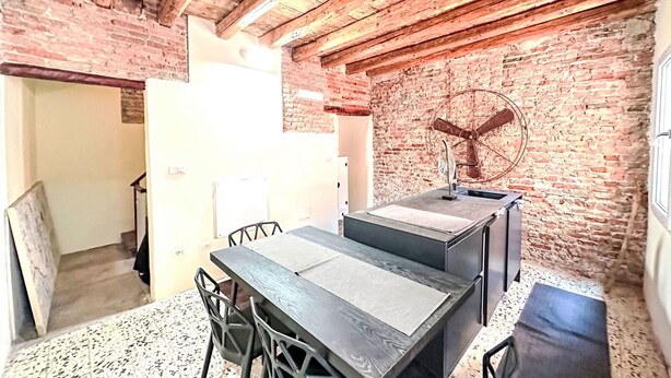 A rustic dining area with a brick wall, wooden ceiling beams, and a vintage fan. - La Casa di Cri' by Interhome (Chioggia)