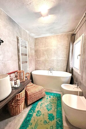 Ein modernes Badezimmer mit einer freistehenden Badewanne, einem Waschtisch mit Spiegel und einem kleinen Waschbecken.