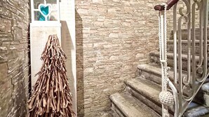A stone-walled staircase with a metal railing, a wooden beam ceiling, and a decorative arrangement of branches and a heart-shaped object on a white stand. - La Casa di Cri' by Interhome (Chioggia)