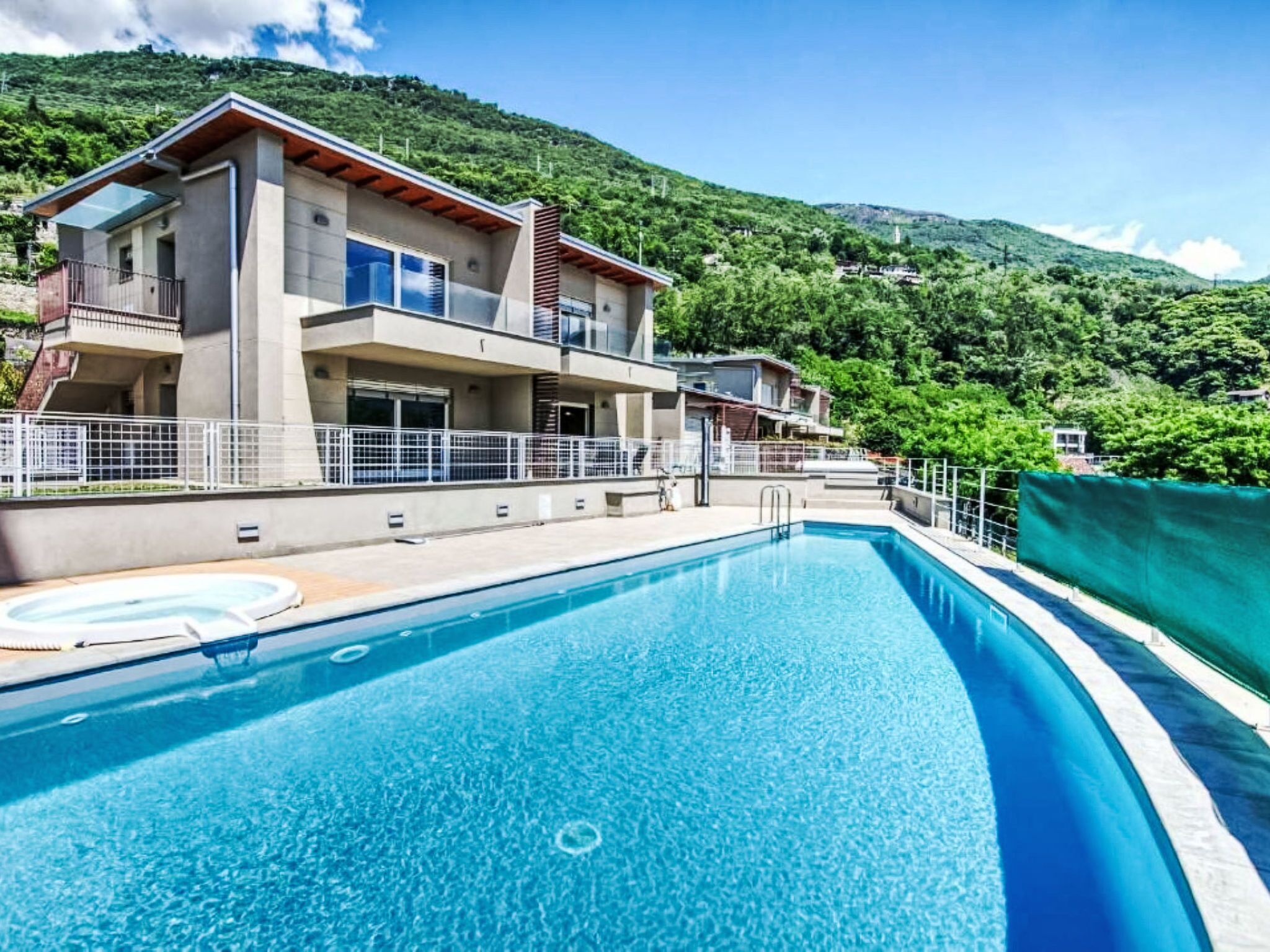 A modern two-story building with a swimming pool, surrounded by lush green hills.