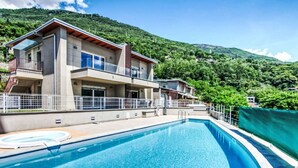 A modern two-story building with a swimming pool, surrounded by lush green hills.